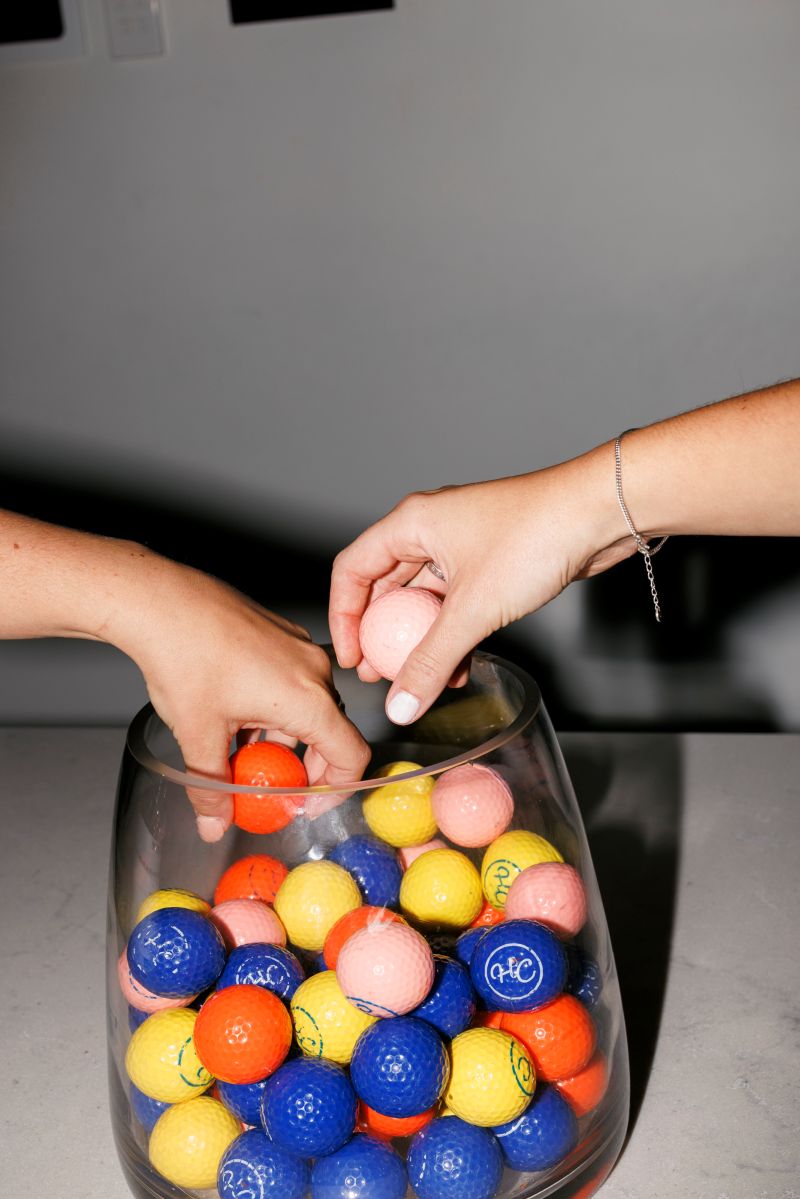  Two hands reaching toward a bowl filled with vibrant, colorful balls of various sizes.