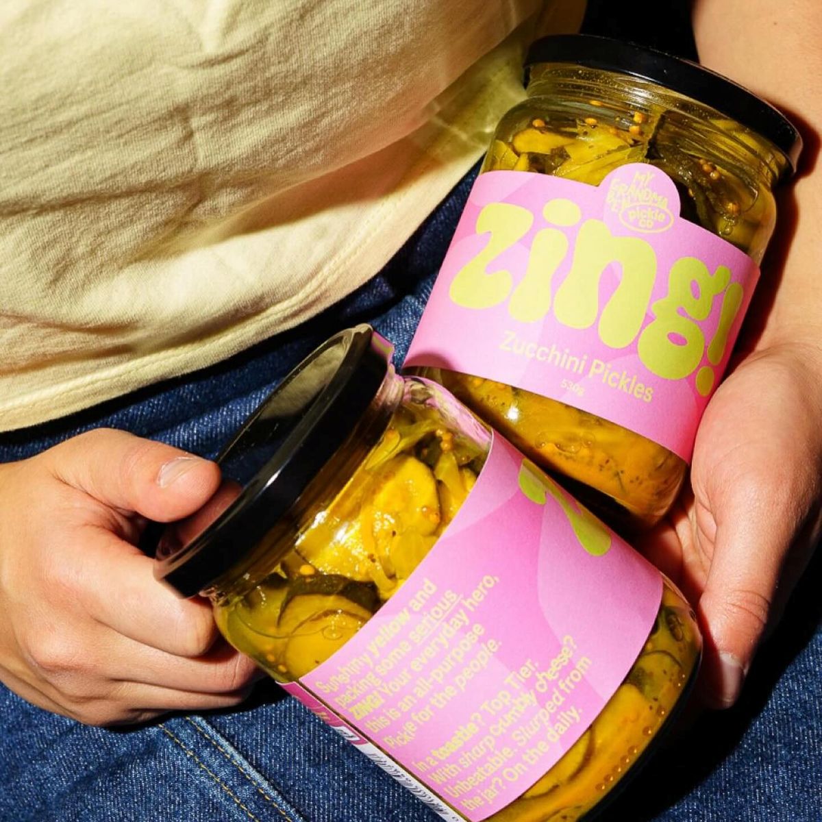 A woman holds two jars of pickles, showcasing her homemade preserves.