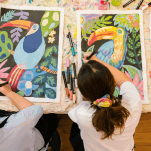 Two girls are engaged in painting on canvases, showcasing their creativity and collaboration in an artistic setting.