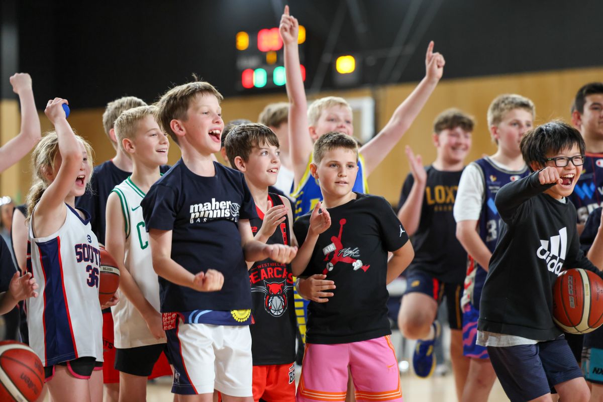A group of young boys and girls enthusiastically playing basketball on an outdoor court.