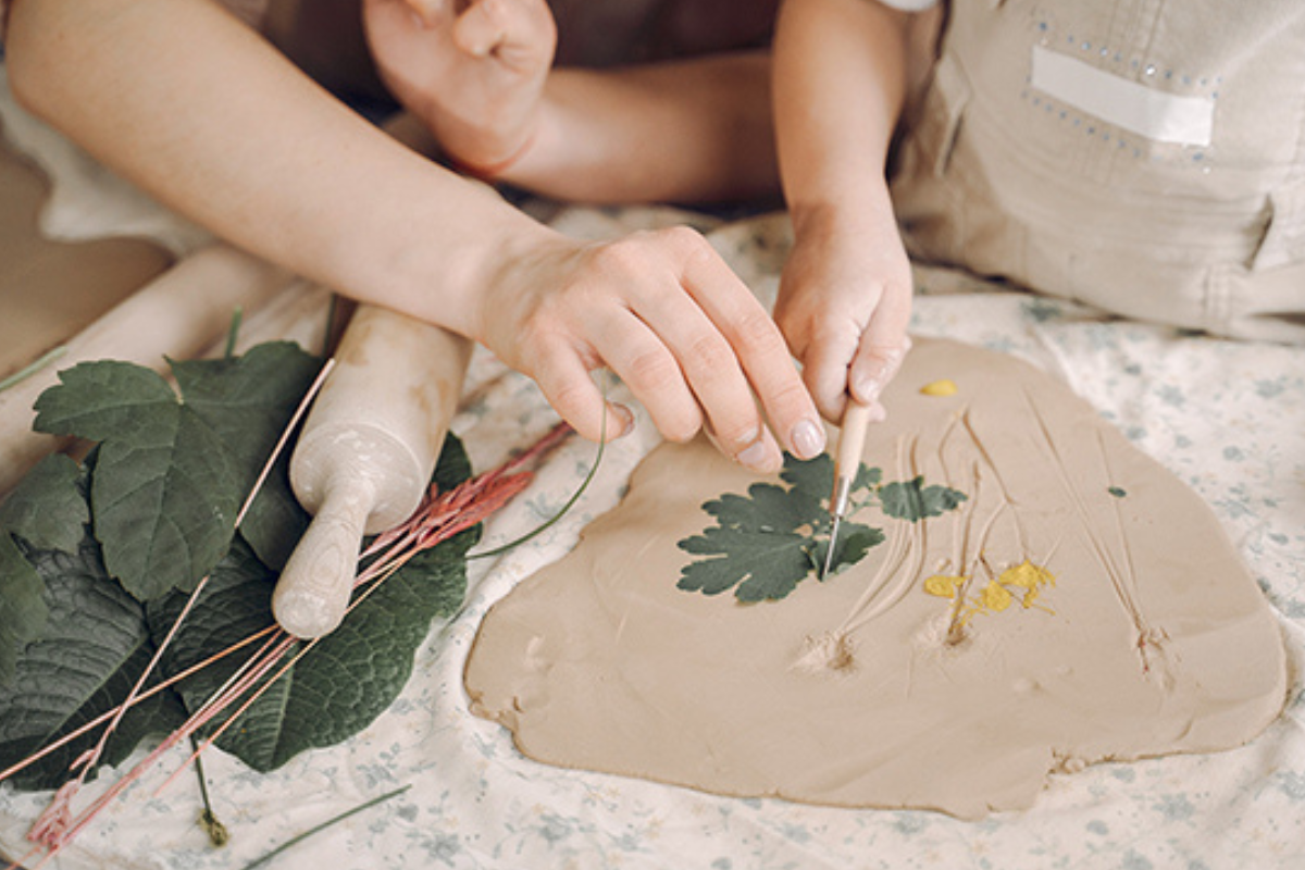 A woman and a child are crafting clay using leaves, showcasing a creative and playful activity together.
