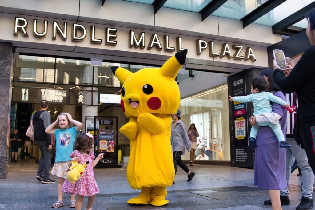 A person in a Pikachu costume stands before a crowd, smiling and engaging with the audience at a lively event.