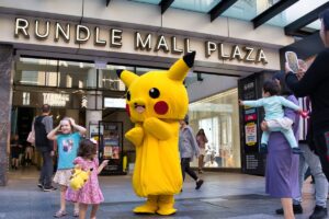 A person in a Pikachu costume stands before a crowd, smiling and engaging with the audience at a lively event.