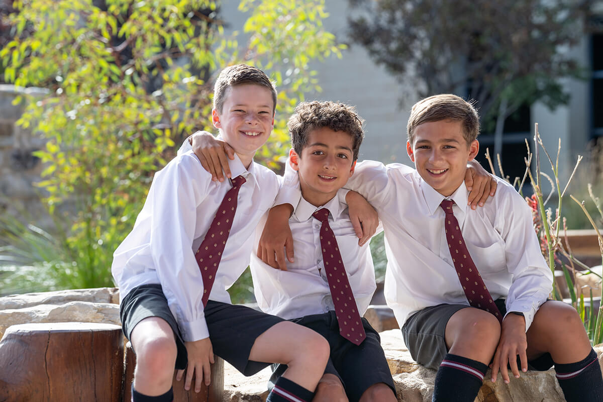 Three boys in school uniforms sitting together on a bench, engaged in conversation and enjoying their time outdoors.
