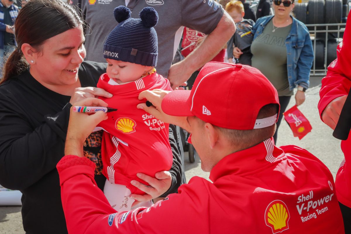Race car driver signing autograph on baby.