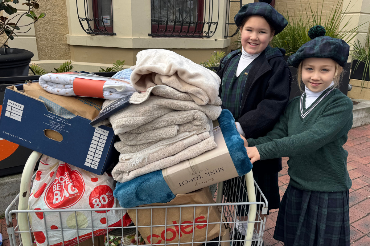 Two young girls in school uniforms smiling while pushing a shopping cart together.
