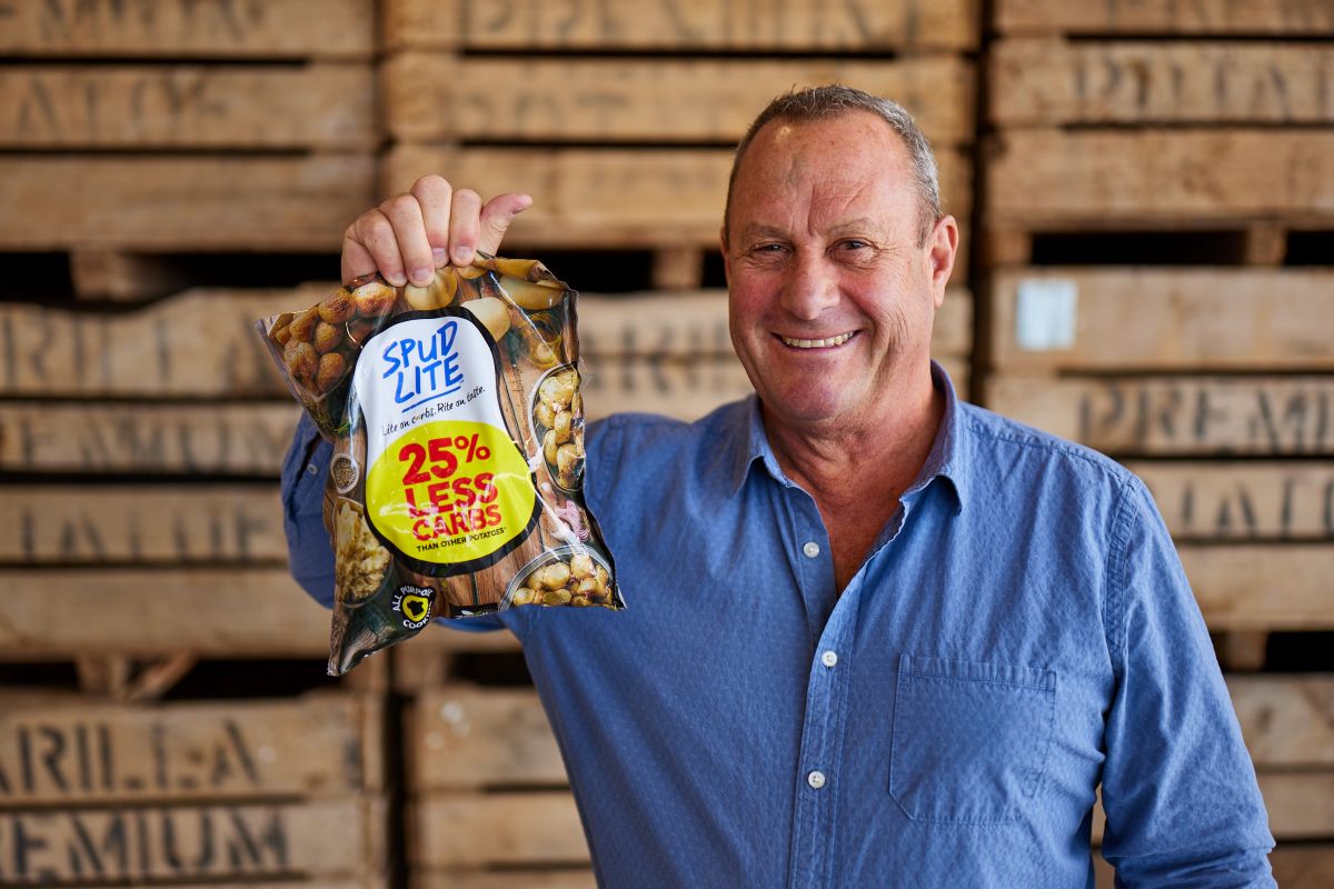 Man smiles at camera, holding a bag of potatoes