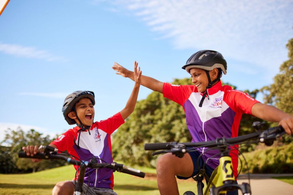Two boys on bikes share a high five, celebrating their friendship and playful spirit in a sunny outdoor setting.