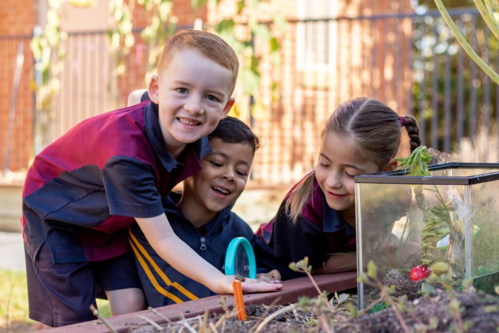 Three children are gathered around a fish tank, observing the fish and interacting with the water and decorations inside.