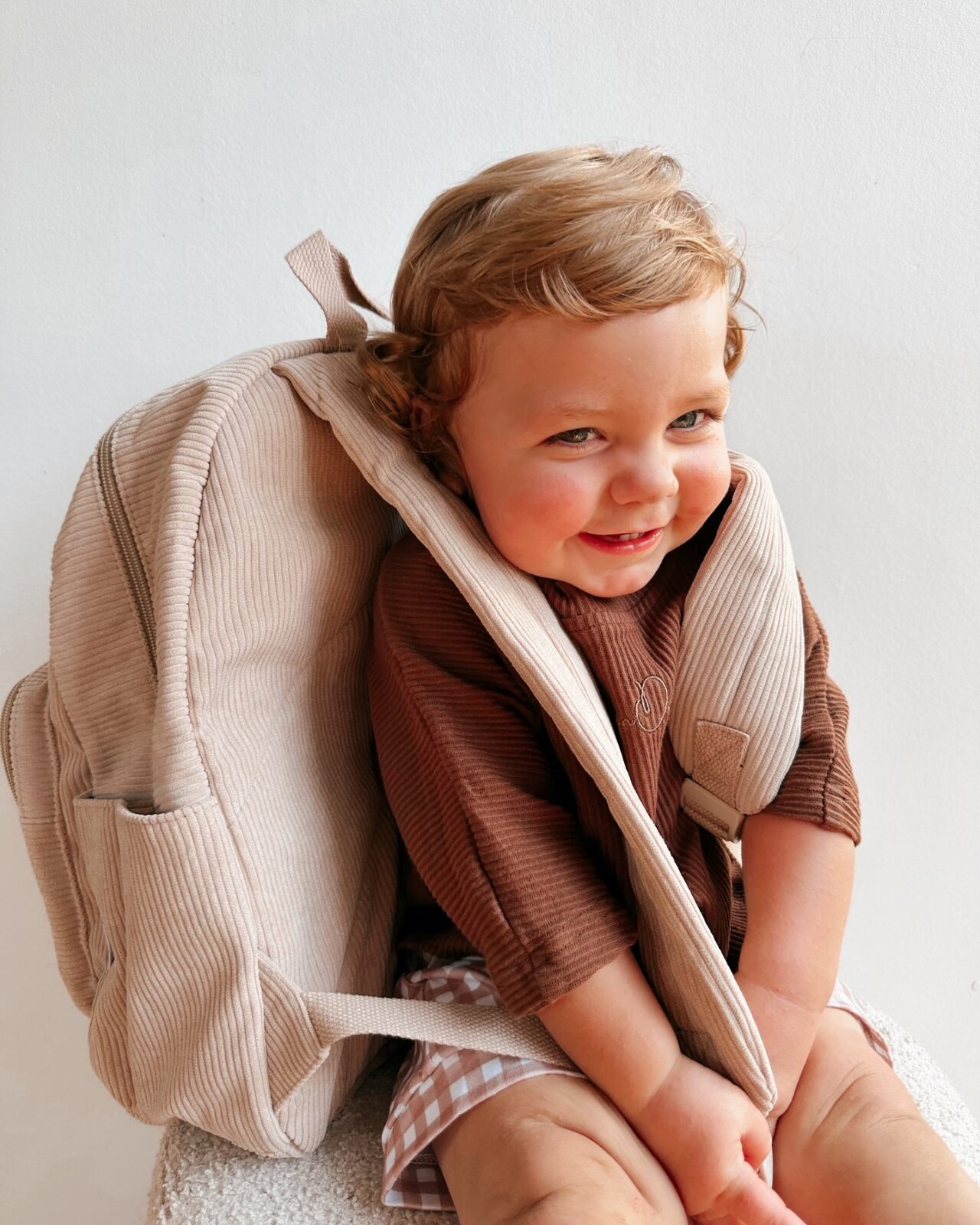 A toddle smiles with a backpack on his back.