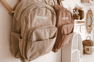 Two backpacks hanging on a wall in a room, showcasing different colors and styles.