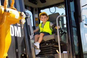 A young boy sitting on a bright yellow construction vehicle, smiling and enjoying the view from the driver's seat.