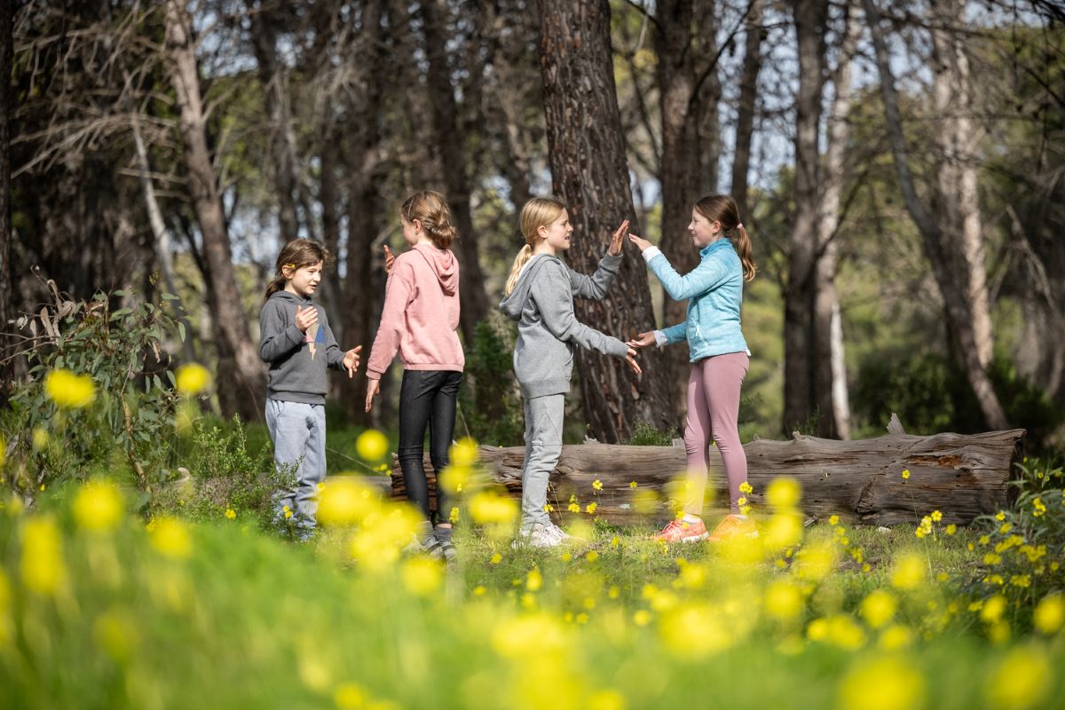 Four children stand in a vibrant field filled with blooming yellow flowers, smiling and enjoying the sunny day.