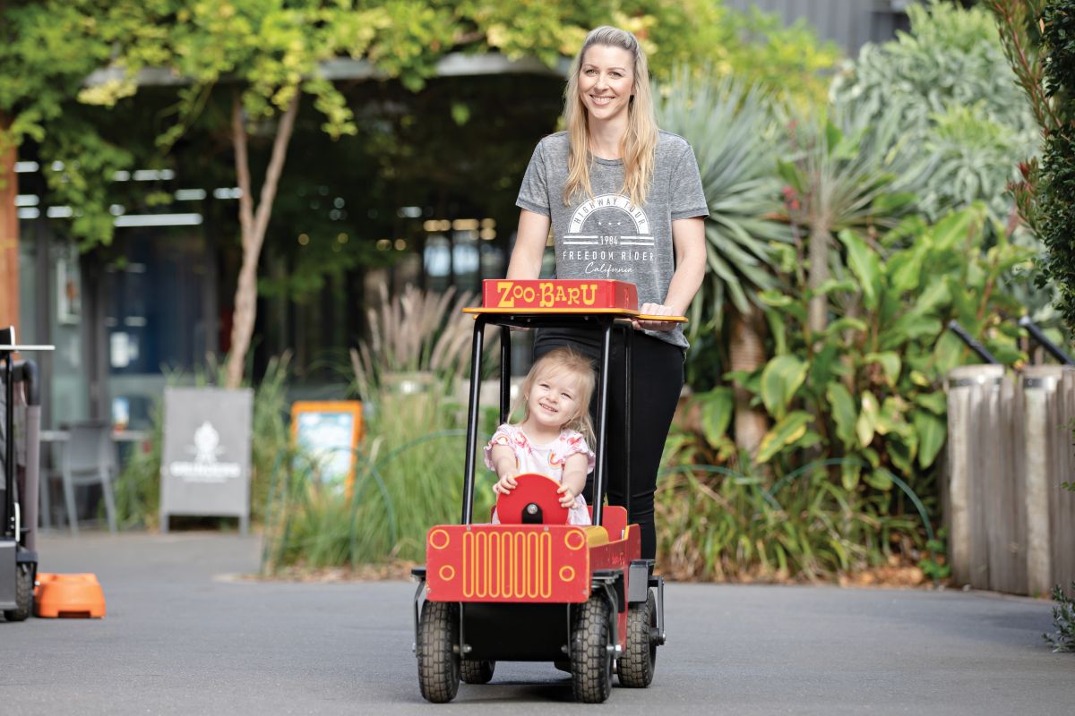 A woman and a child happily riding together in a bright red toy car.