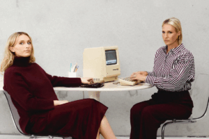 Two women seated at a table, collaborating on a computer, engaged in discussion and sharing ideas.