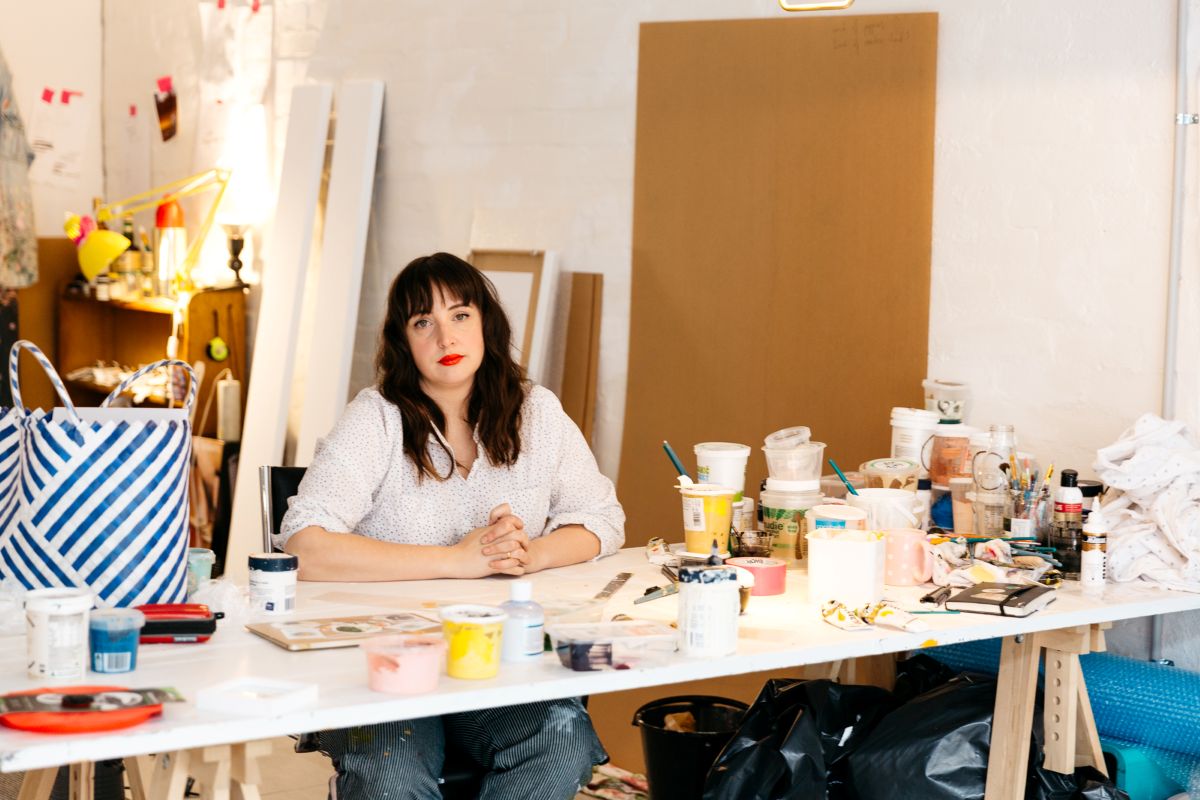 A woman seated at a table surrounded by various supplies, focused on her work.