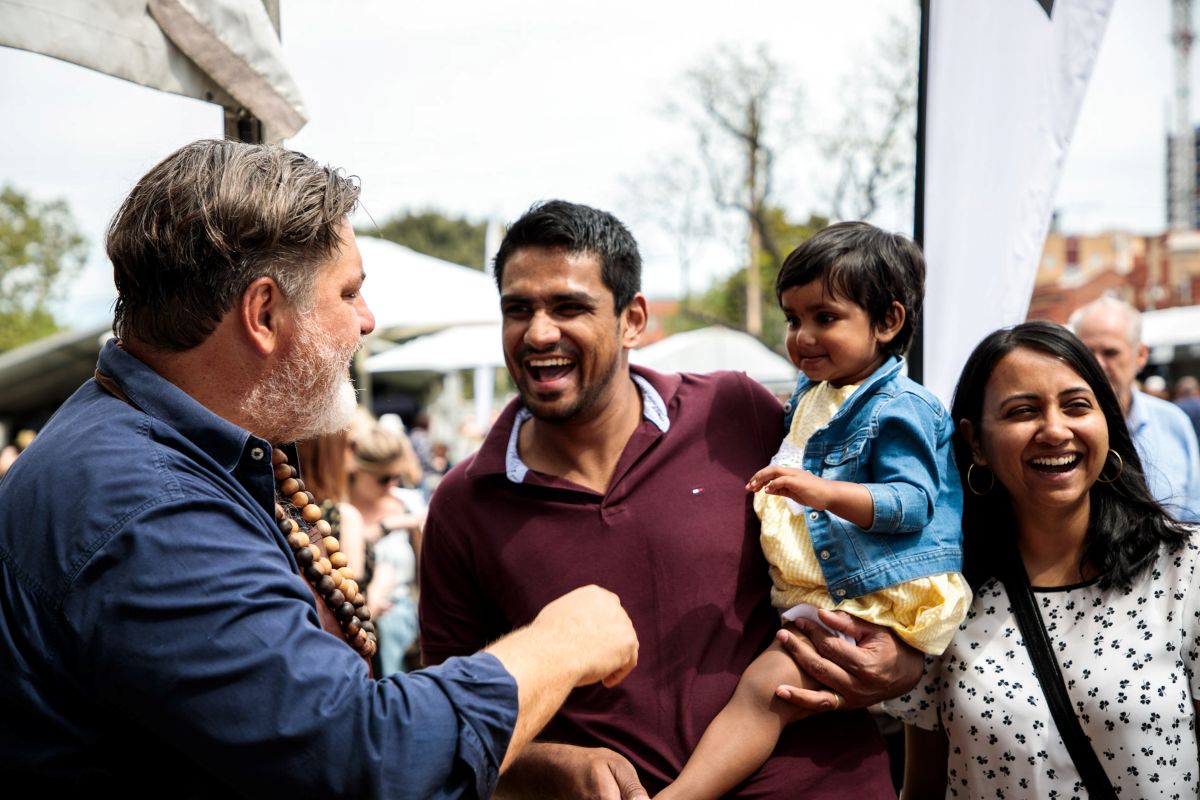 A man and woman with a child enjoying an outdoor event, surrounded by greenery and other attendees.