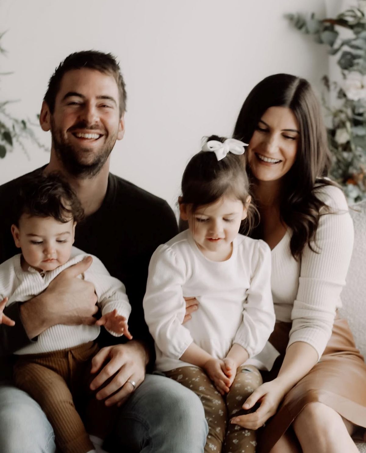 A family of four, including two children, sitting together on a cozy couch in a warm living room setting.