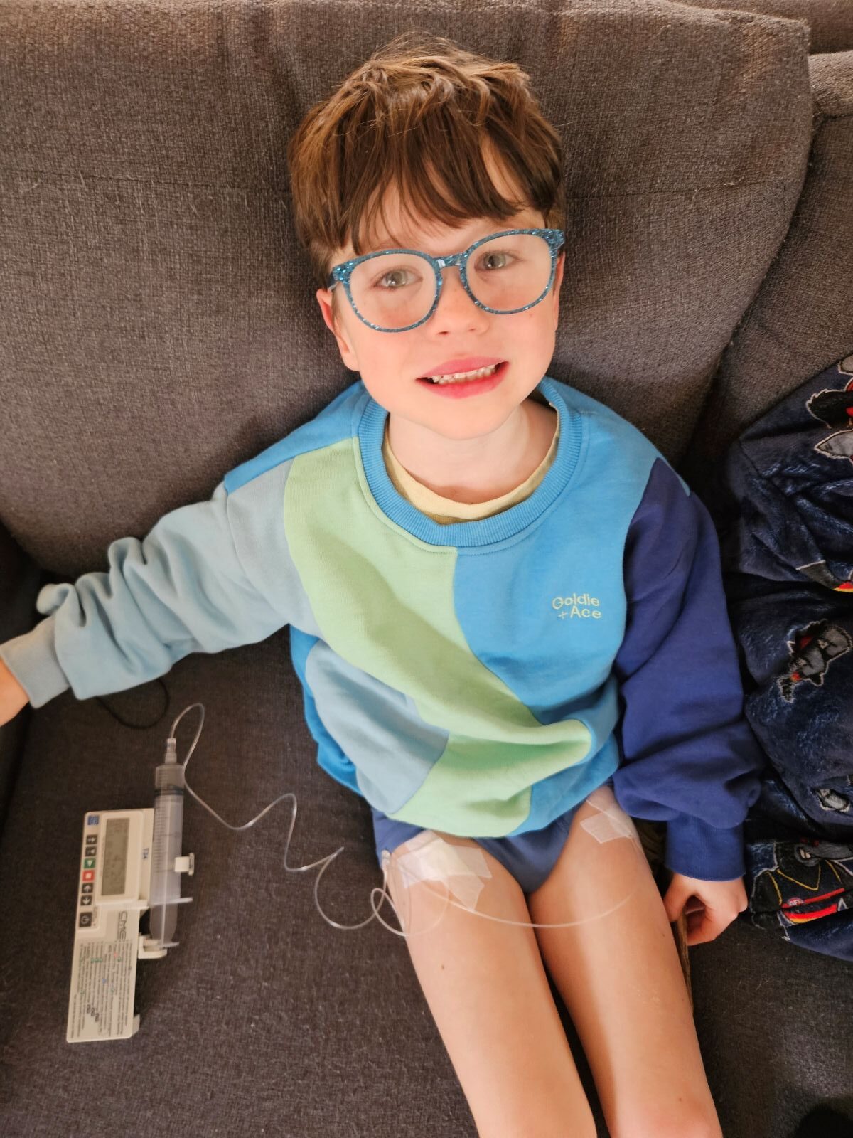 A young boy with glasses is relaxing on a couch, looking comfortable and content.