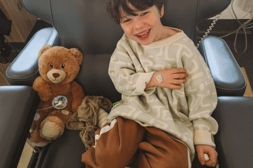 A young boy sitting in a chair, holding a teddy bear close to him, with a gentle smile on his face.