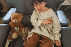 A young boy sitting in a chair, holding a teddy bear close to him, with a gentle smile on his face.