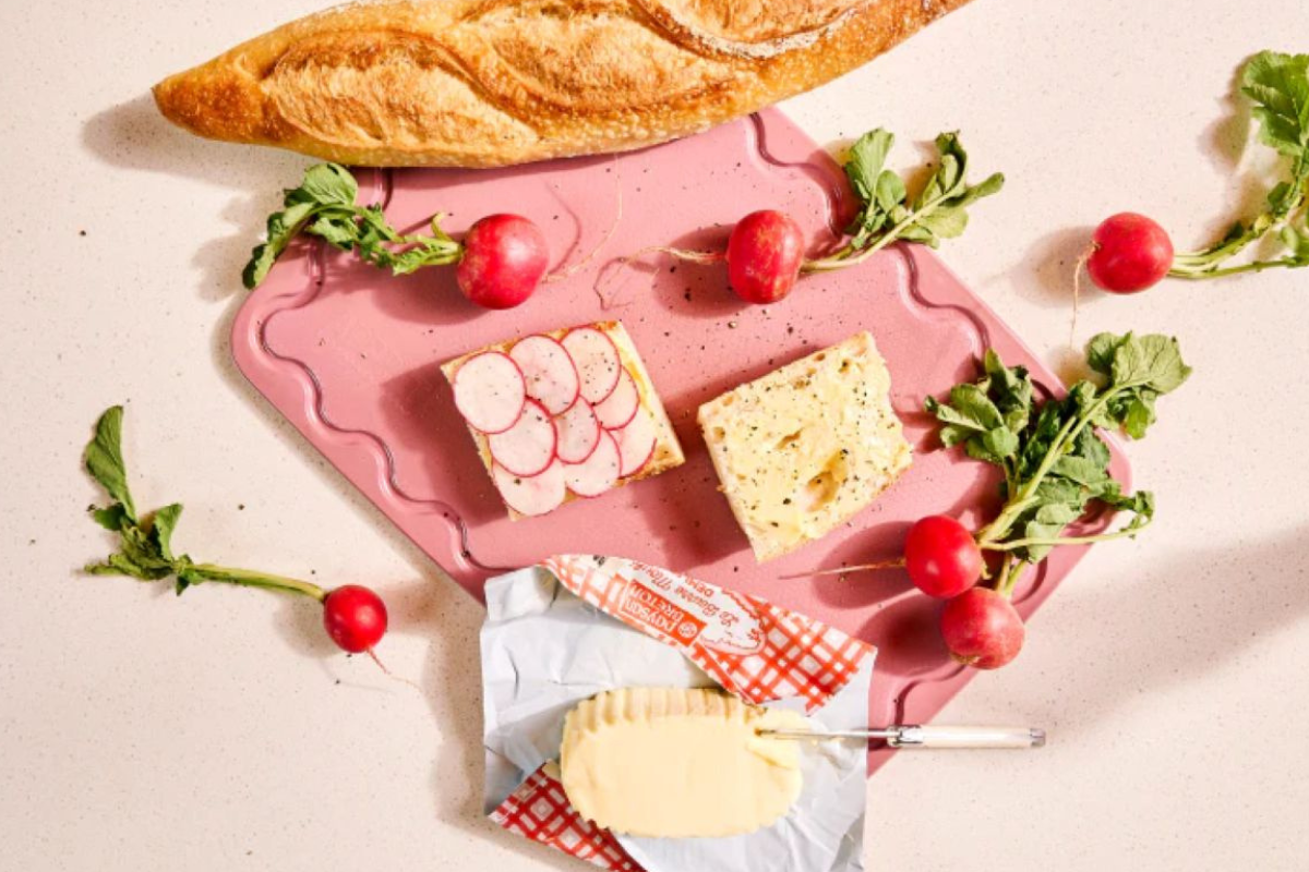 A pink cutting board displaying sliced radishes next to a loaf of bread.