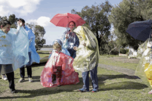 A group of people wearing colorful raincoats stands together, smiling under a cloudy sky.