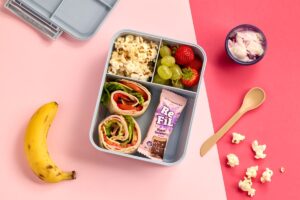 A lunch box filled with assorted fruit, nuts, and a ripe banana arranged neatly inside.