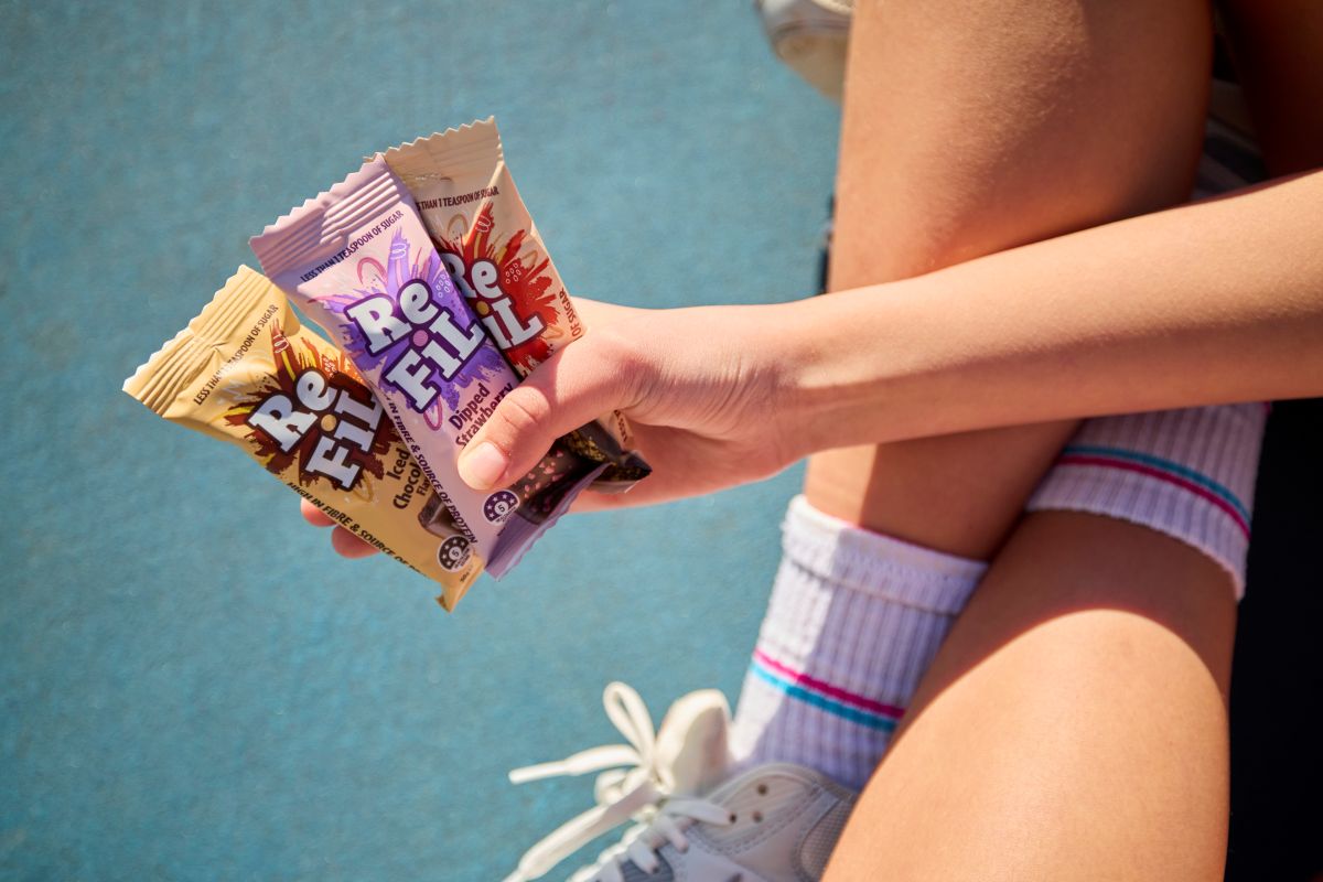 A person sitting on a bench, casually holding a bag of snacks in their hands.