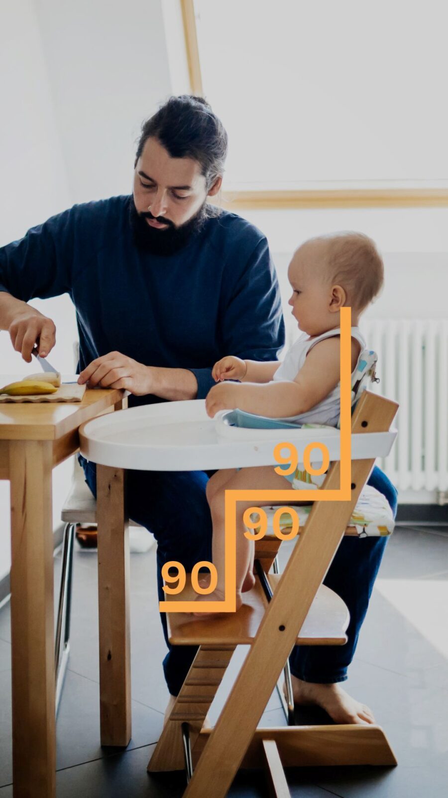  A man sits beside a baby in a high chair, both smiling and enjoying a moment together.