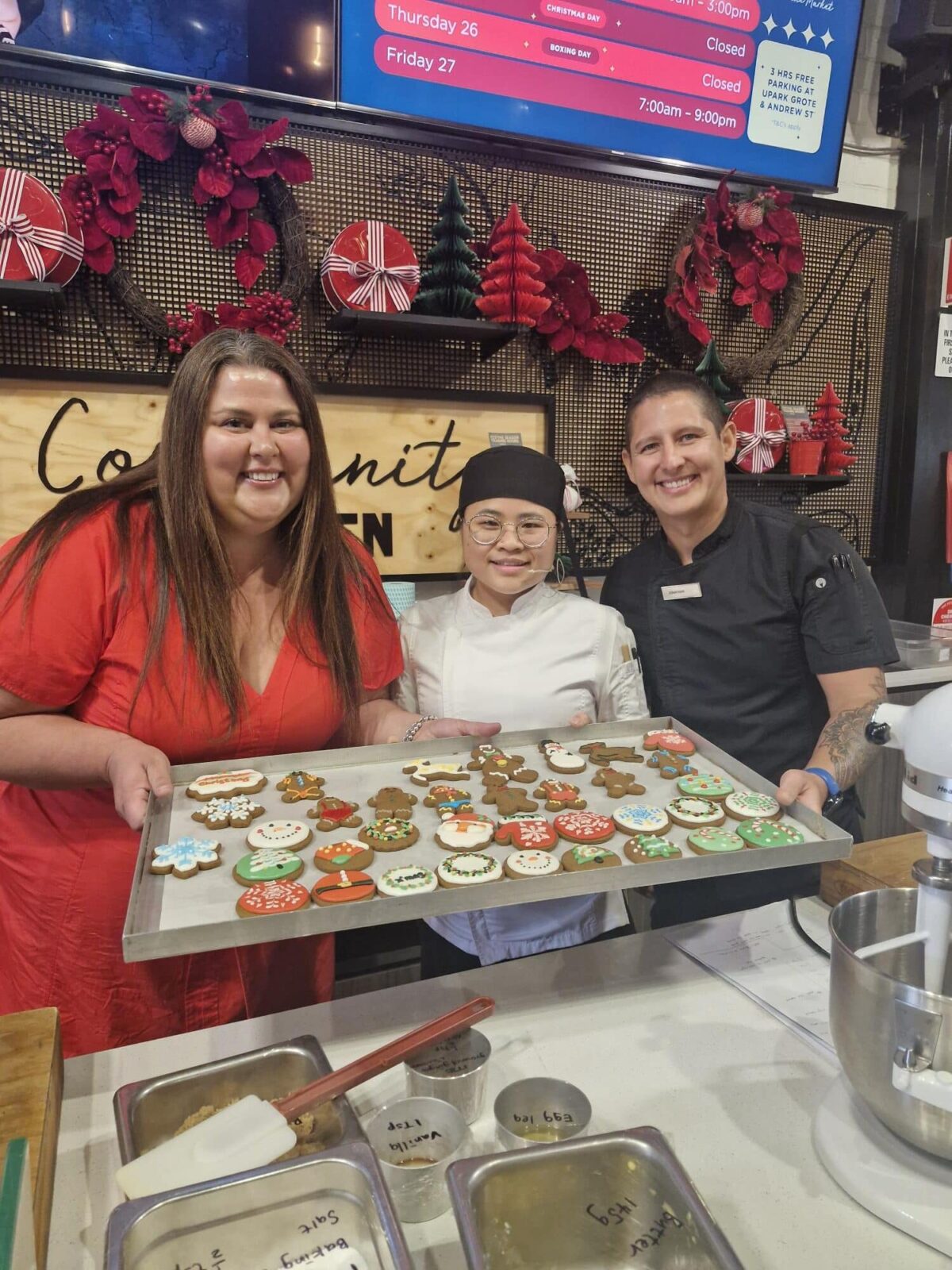 A woman and two children proudly hold a tray of freshly baked cookies together.