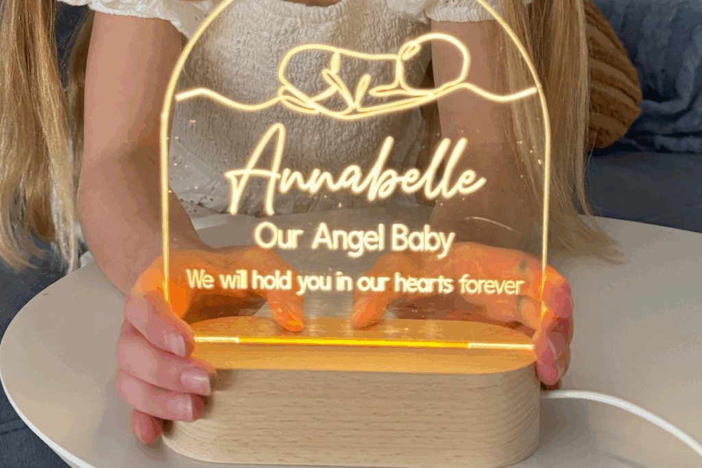 A girl holds a lit lamp inscribed with the words "our angel baby," symbolizing remembrance and love.