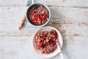 Two bowls of chia pudding topped with fresh strawberries and cherries, arranged on a wooden table.
