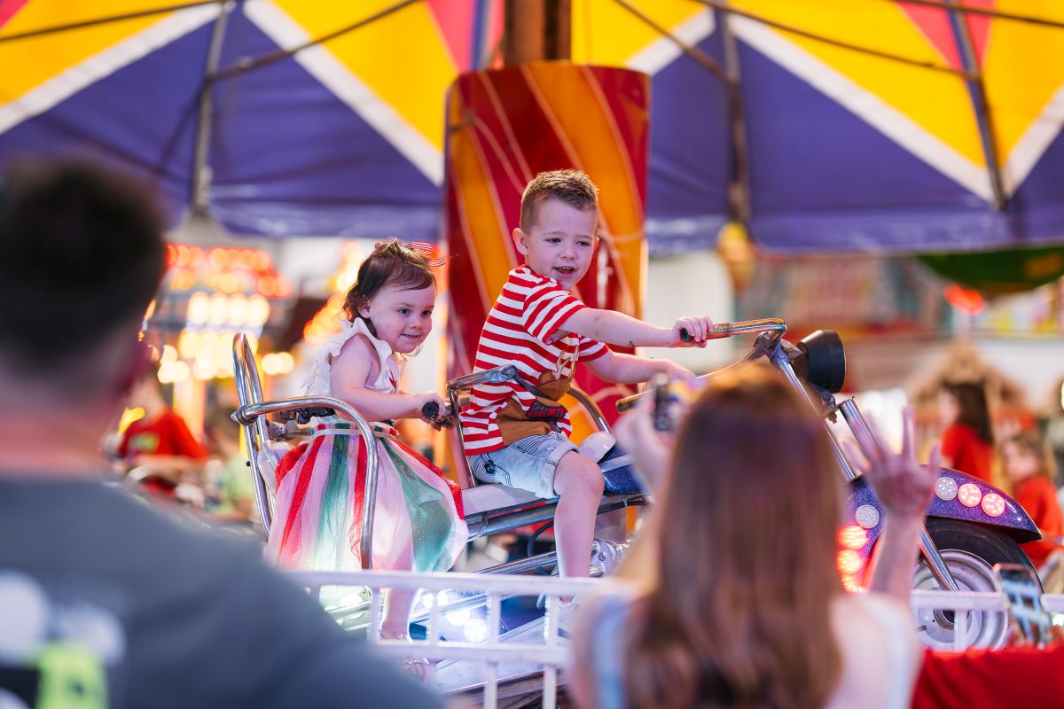 A young boy and girl smiling as they enjoy a colorful carnival ride together. 