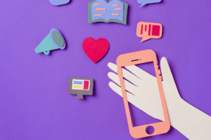 Hand holding a smartphone displaying social media icons on a purple background, representing digital connectivity.