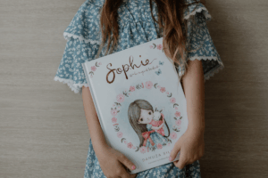 A girl holding the book Sophie's Magical Backpack.