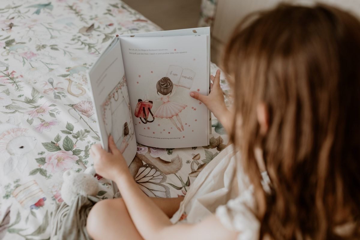  A little girl sits on her bed, happily reading a book with colorful illustrations.