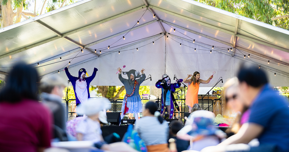 A group of performers in colorful costumes stands on stage, engaging the audience with their lively presentation.