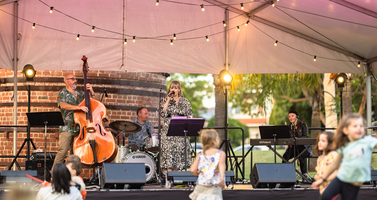 A group of jazz musicians playing instruments together under a large tent at an outdoor event.