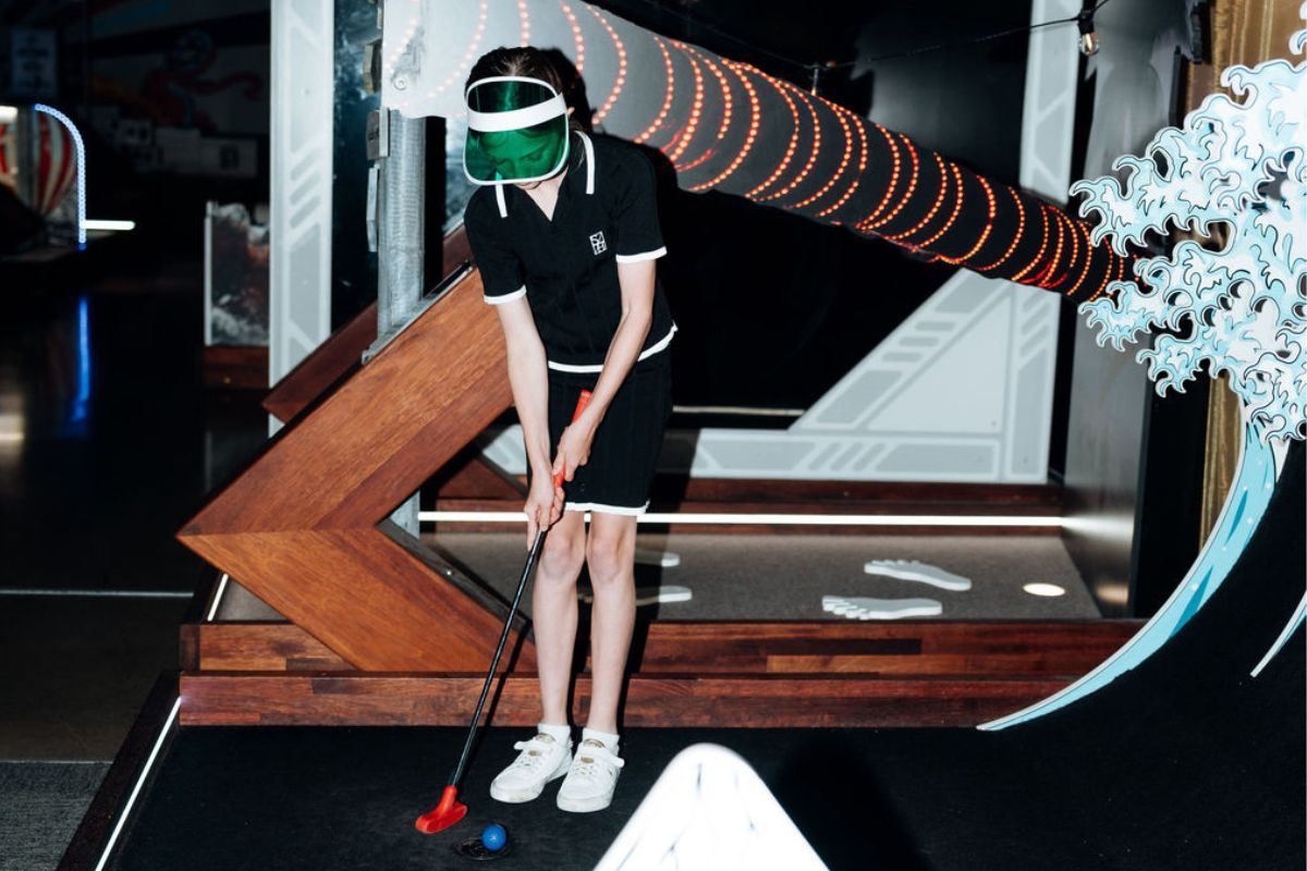 A child in a black shirt swings a golf club on an indoor golf course.