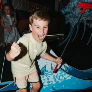 A young boy enjoys playing mini golf at a vibrant theme park, focused on his next shot.