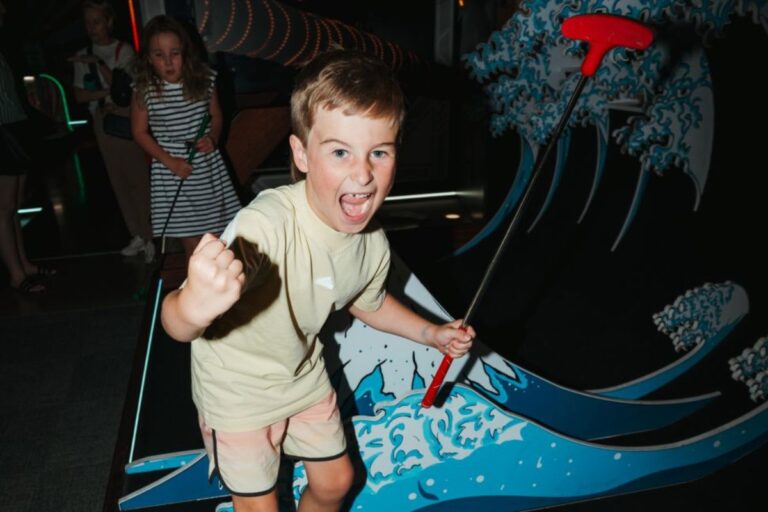A young boy enjoys playing mini golf at a vibrant theme park, focused on his next shot.
