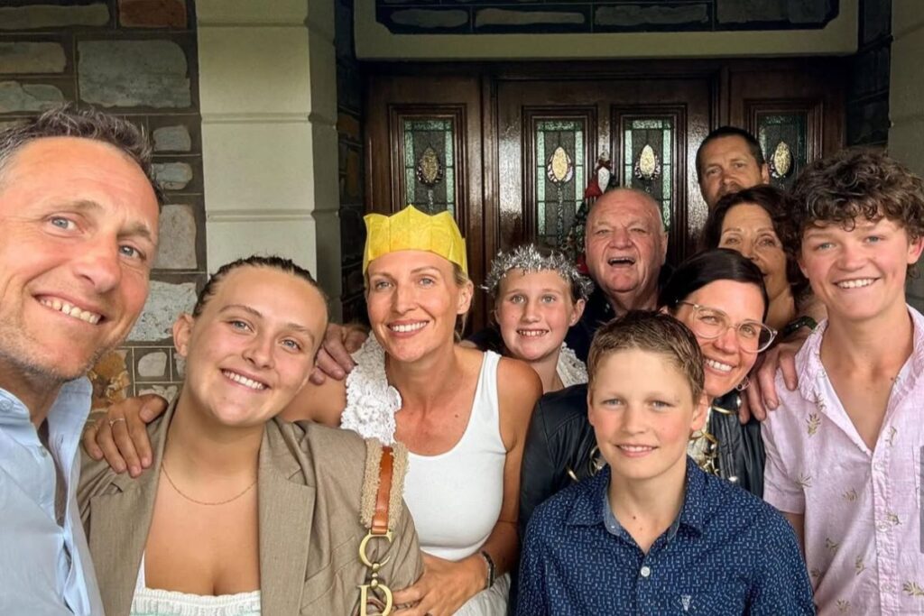 A family gathers for a photo outside their house, capturing a moment of festive joy and unity in a residential setting.