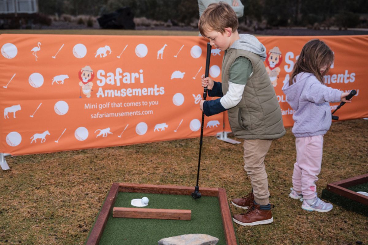 Two children enjoy playing mini golf at Safari Celebrations, surrounded by colorful decorations and themed obstacles.