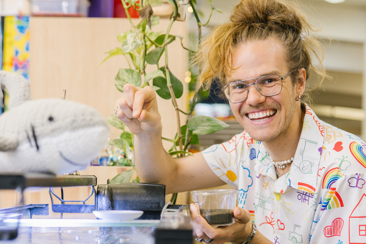 A man smiles while feeding fish in an aquarium. 