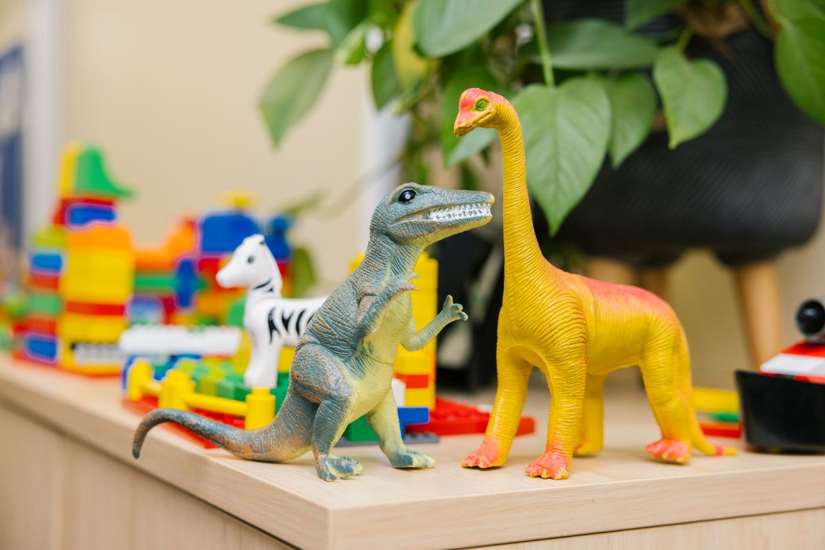 A toy dinosaur and a smaller toy dinosaur displayed together on a wooden shelf.