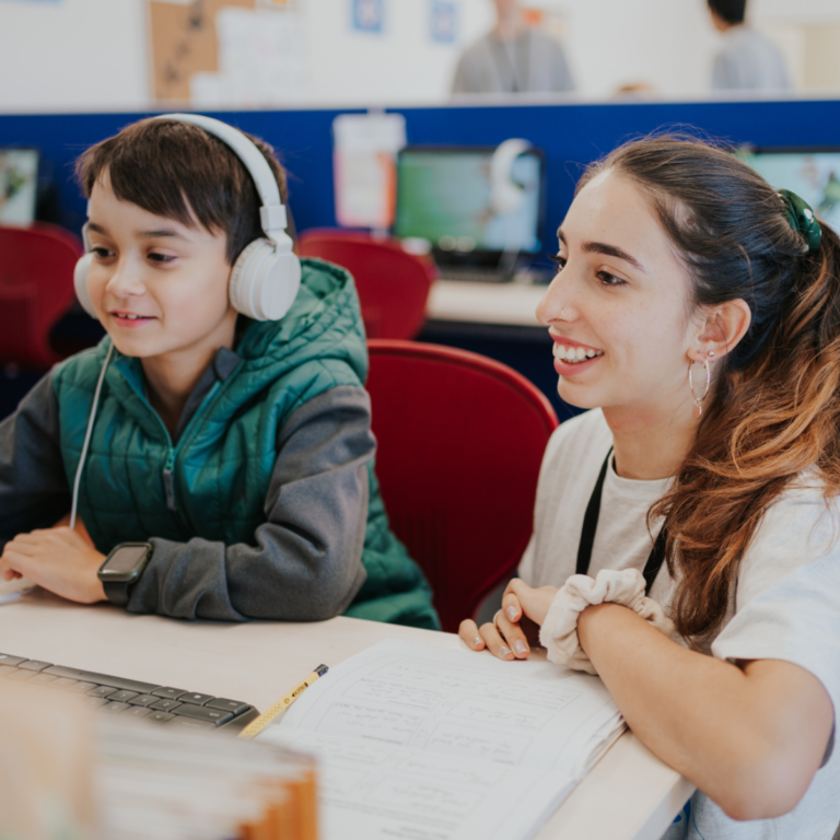 A child wearing headphones and a tutor focus on a computer, engaged in a collaborative learning activity