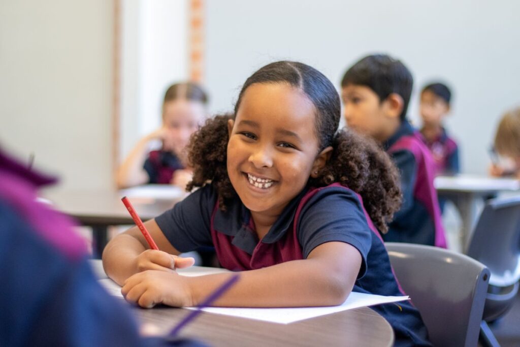 A girl student smiles at the camera, holding a pencil.