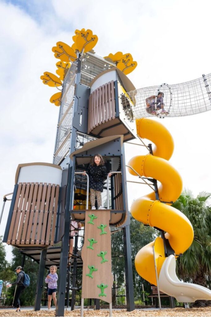 A young child plays on a vibrant yellow slide at a playground, enjoying a sunny day filled with fun and laughter.