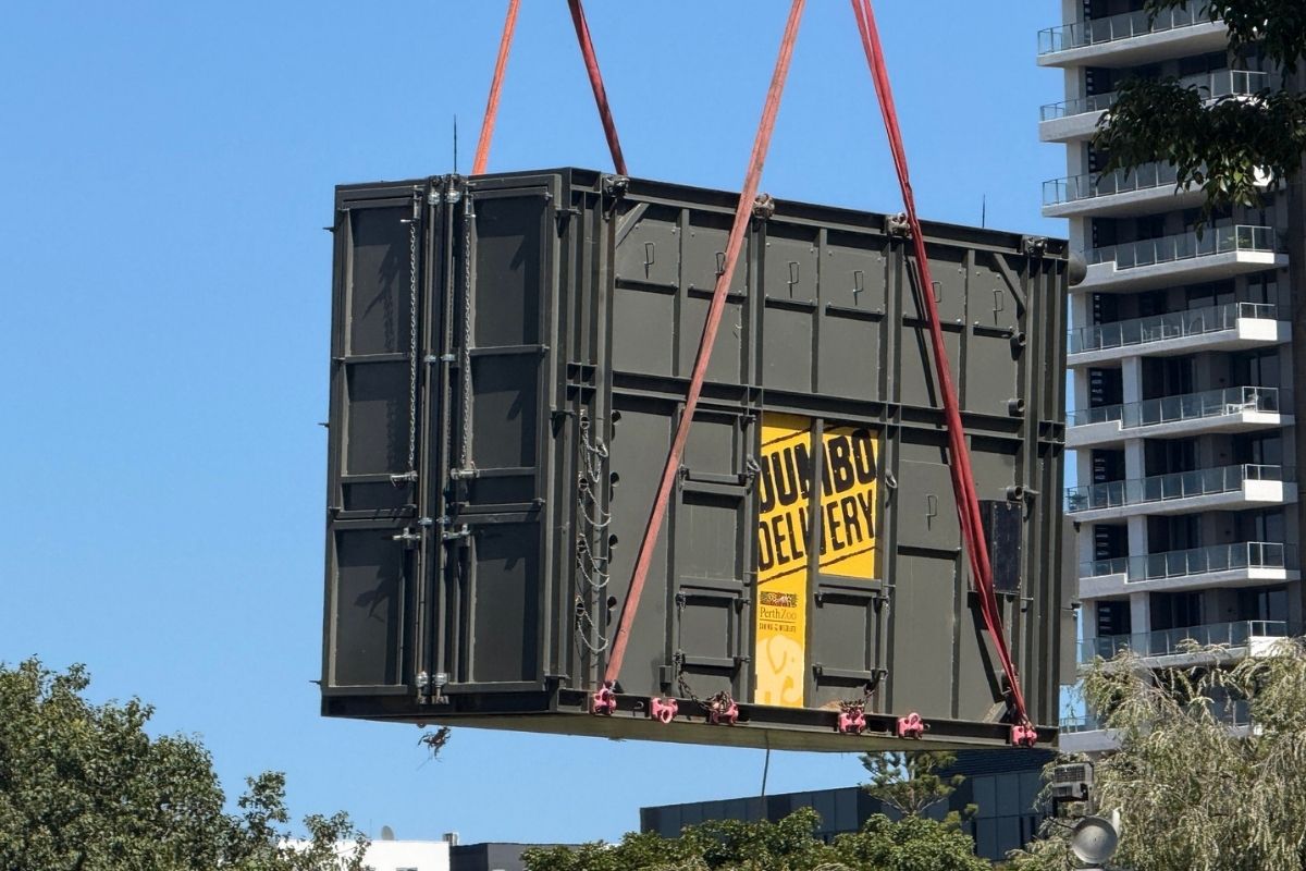 A crane lifts a large container skyward, demonstrating heavy machinery in action at a loading area.